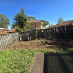 Cleared backyard area with a wooden fence and no visible vegetation.